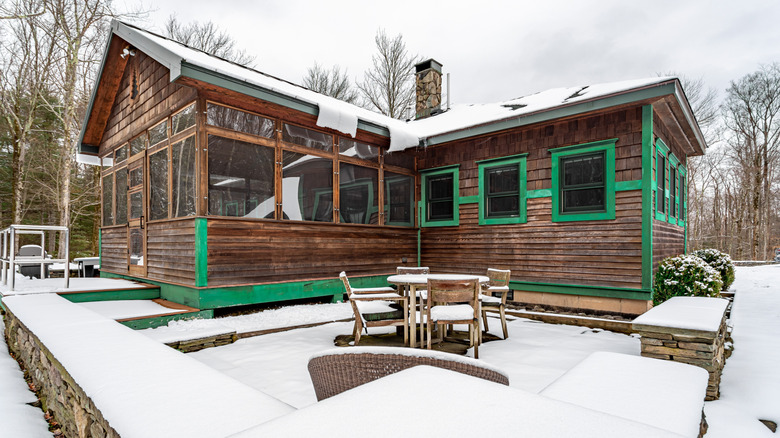 A cute cabin has a deck made unusable from snow.