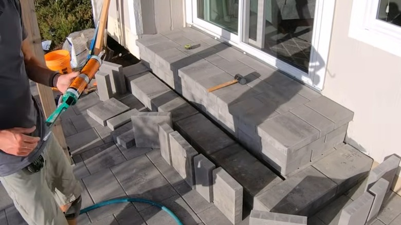 Person holding caulking gun standing next to cement block project leading up to glass doors.