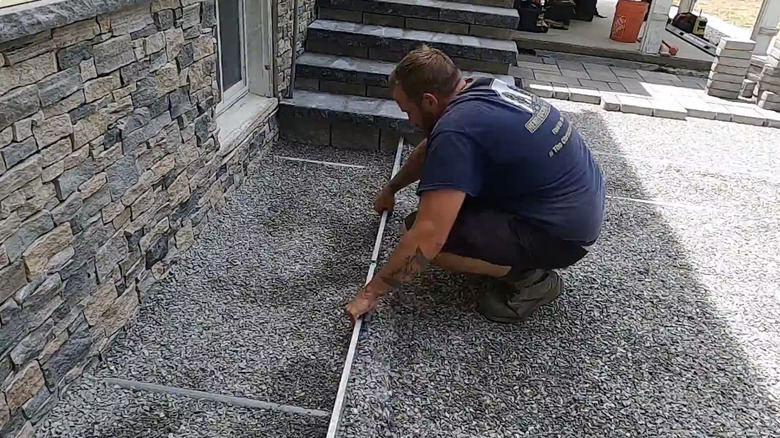 Man levels out crushed stone to finish at the base of a set of concrete block stairs.