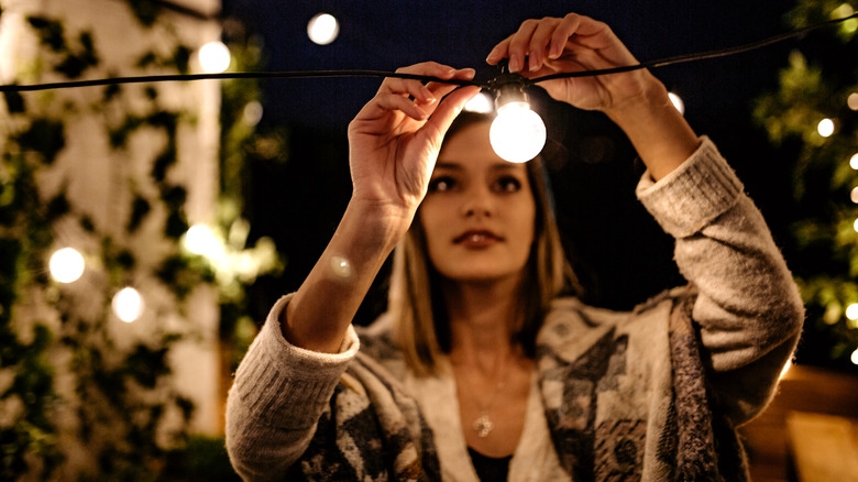 A girl hanging string lights on her patio.