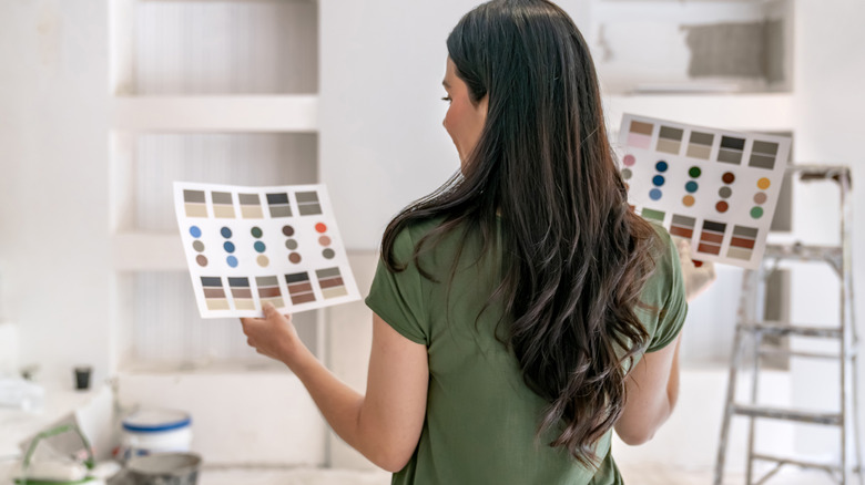Woman holding colorful paint swatches in a white room.