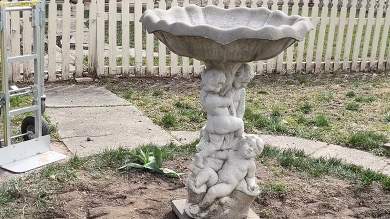 A victorian stone bird bath with baby designs in a yard