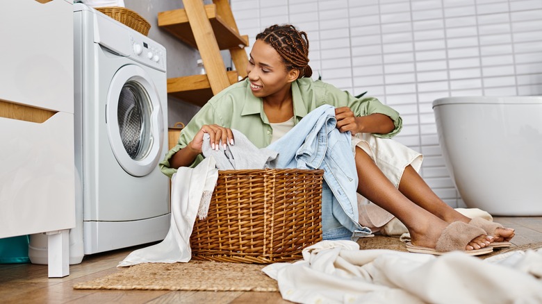 A woman is sitting on the floor in her laundry room with a basket of clothes