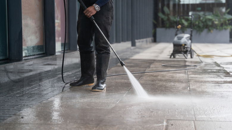 A man using a pressure washer to clean his concrete driveway and patio area.