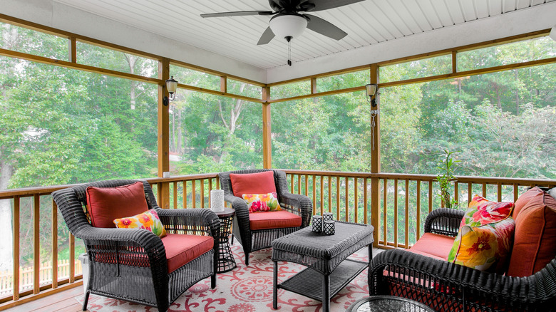 A cozy enclosed porch with ceiling fan and comfortable outdoor furniture