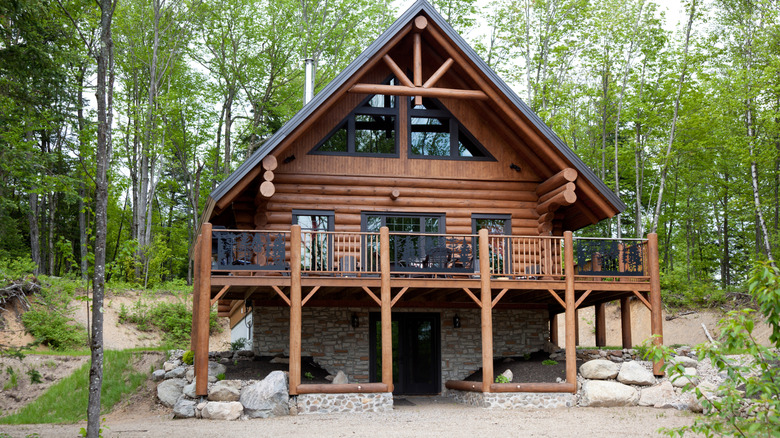 A modern log cabin is in a wooded setting.