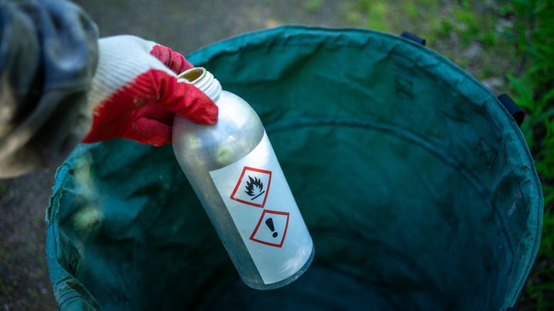 A gloved hand holds a bottle of toxic liquid