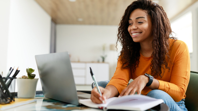 woman working on laptop and taking notes on notepad