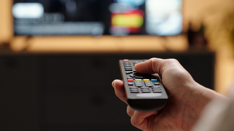 Person's hand holding a TV remote pointed toward the TV