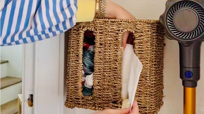 Woman inserts plastic bags into a rattan wall-mounted, double tissue box cover.