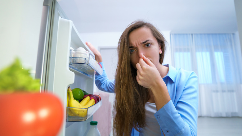 woman plugging nose by refrigerator