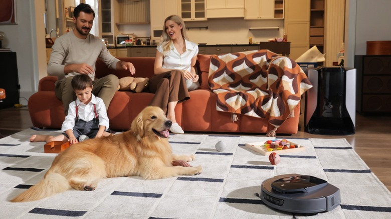 Family with a dog on a couch with a robot cleaner on the carpet