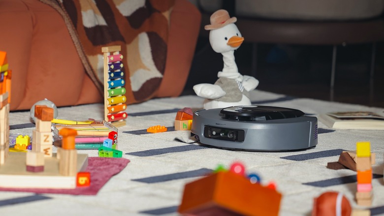Robot cleaner on a carpet surrounded by kids' toys