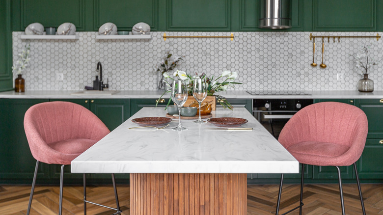 two pink chairs at a breakfast countertop made from stone in a forest green kitchen