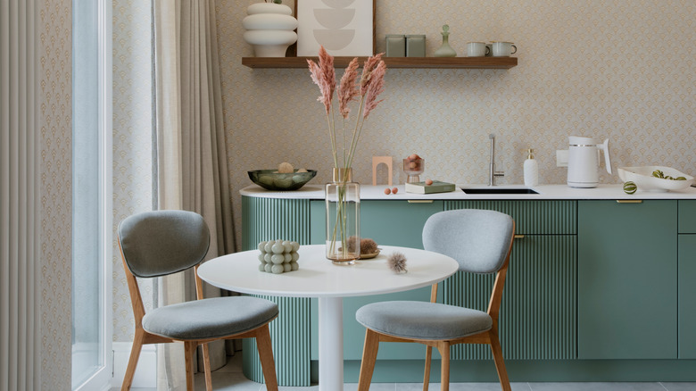 two padded chairs at a round table with a glass vase, candle, glass fruit bowl and designer kettle