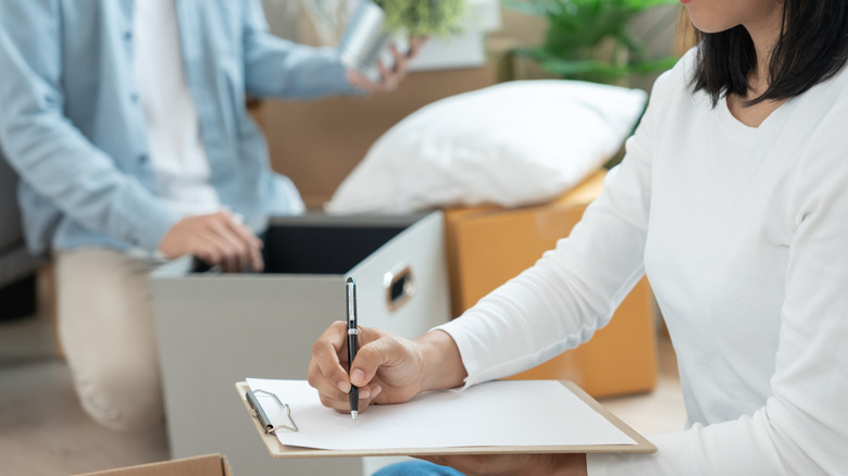 Woman writing checklist while second person considers items to donate or keep