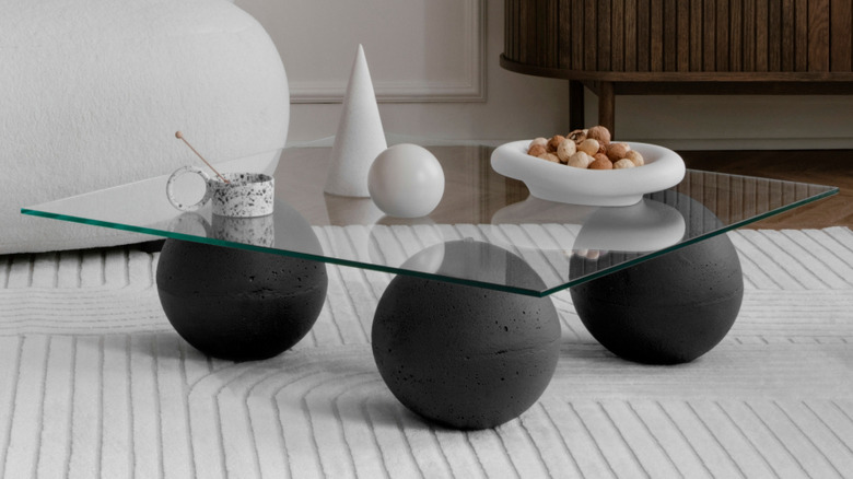 Assymetrical glass top coffee table with black cement ball supports, minimal styling in white on a white textured rug