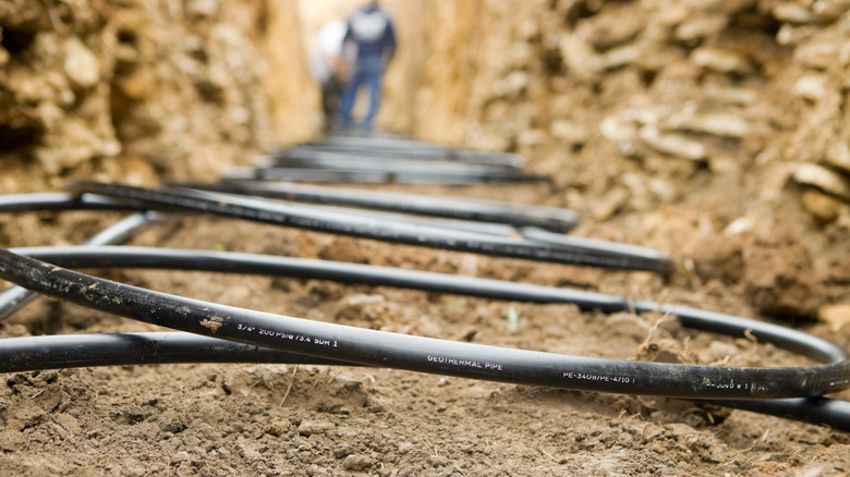 Black pipes are coiled in a trench dug in a yard for a geothermal pump system.