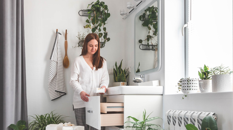 Woman putting bathroom item in a drawer under the sink.