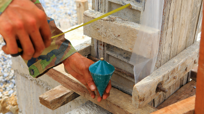 Hands steady a plumb bob to check a pillar's verticality.
