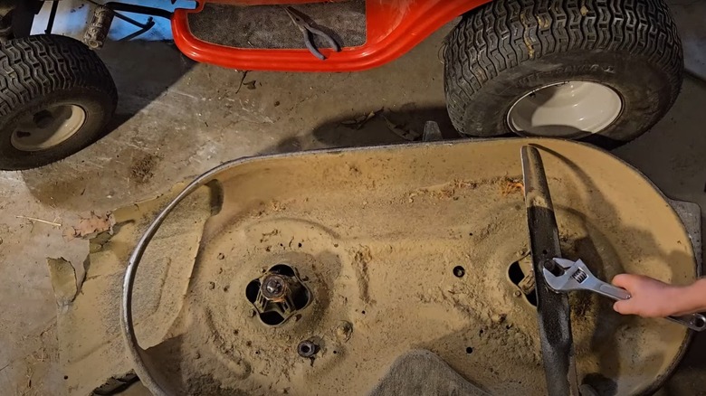 Person using a wrench to loosen riding mower blades