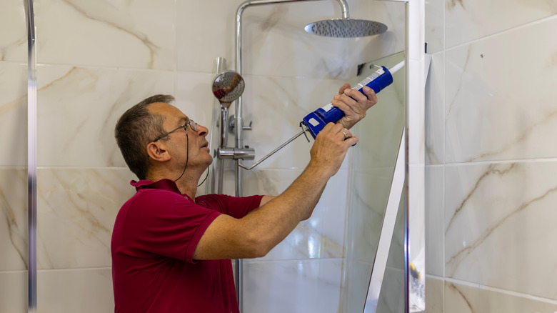 Man applying silicone caulk to seal the edge of a glass shower partition.