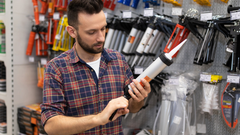 Man shopping for caulk and caulk gun at a hardware store.