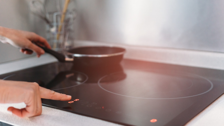 A person uses an induction cooktop with a pan