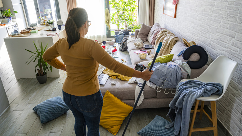 Woman holding a mop, contemplating her messy and cluttered living space