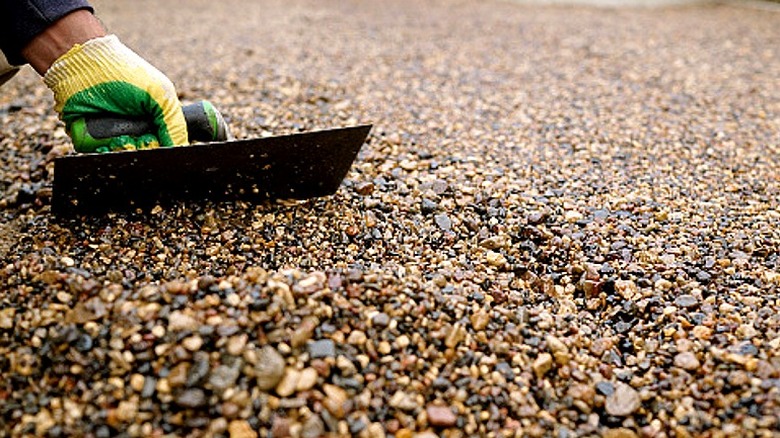 Close-up of a person's hand using a tool to go over a wet gravel surface
