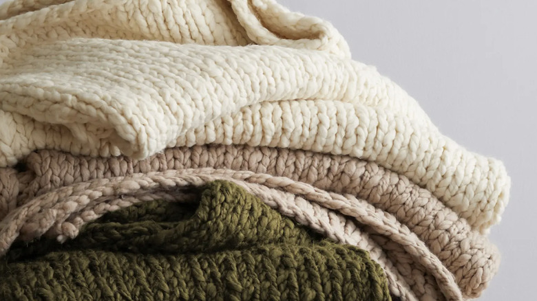 Stack of various neutral colored Chunky Hand Knit Wool Throw blankets from Quince
