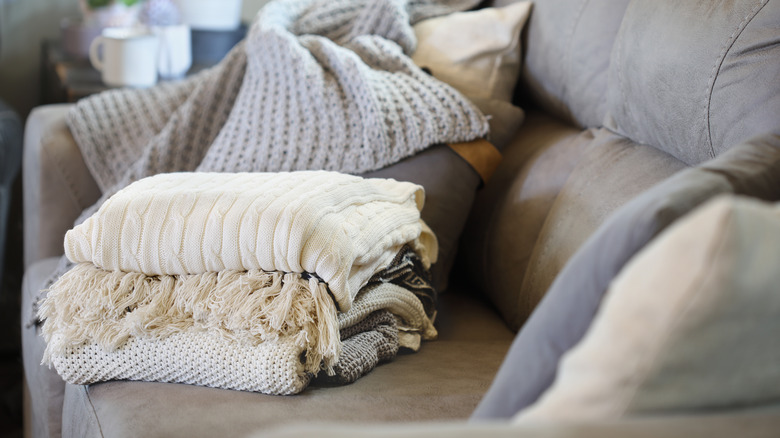Stack of various knit blankets sitting on a gray couch