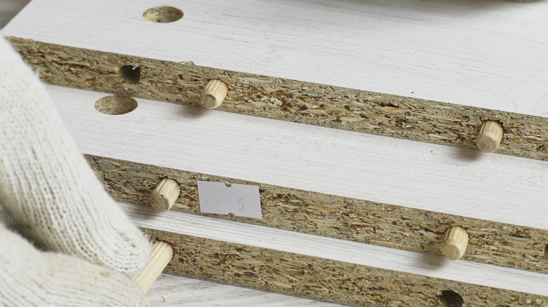 MDF cabinet material close up with worker applying wooden dowels