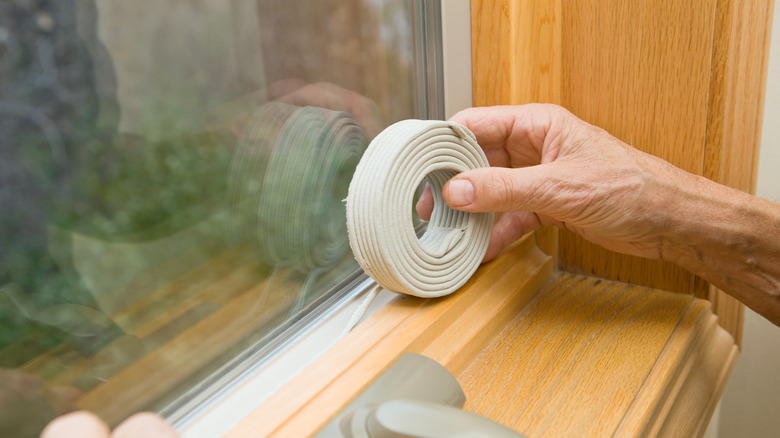 Hand applying weatherstripping to window