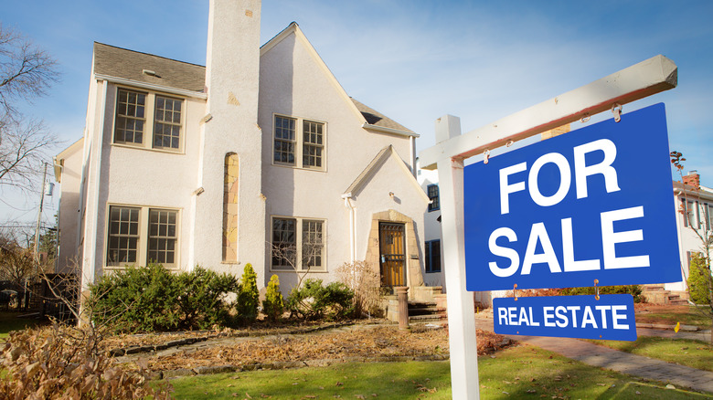 A classic Tudor style house in the mid-west of United States for sale with sale sign on lawn. The two stories property with an old world facade, featuring a fire place chimney.