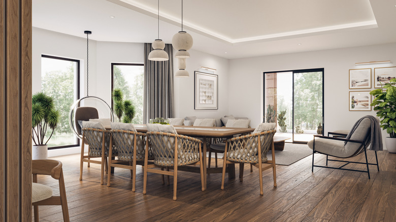 Open space living room and kitchen interior with large windows, TV wall, gray sofa, dining table and hardwood flooring.