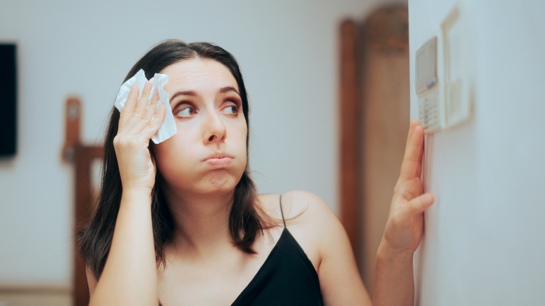 Woman adjusting thermostat while wiping her face with a tissue