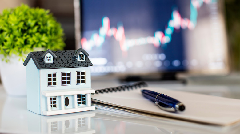small house figurine sitting next to computer with pad and pen