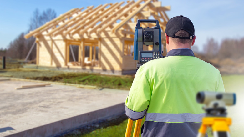 A surveyor wearing a hi-visibility jacket measuring the property line for a fence in front of a partially constructed home