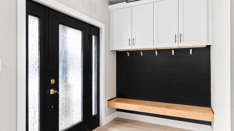 A modern farmhouse entryway with bench seating, black shiplap, white cabinets, gold coat hooks, and a black and gold light fixture.