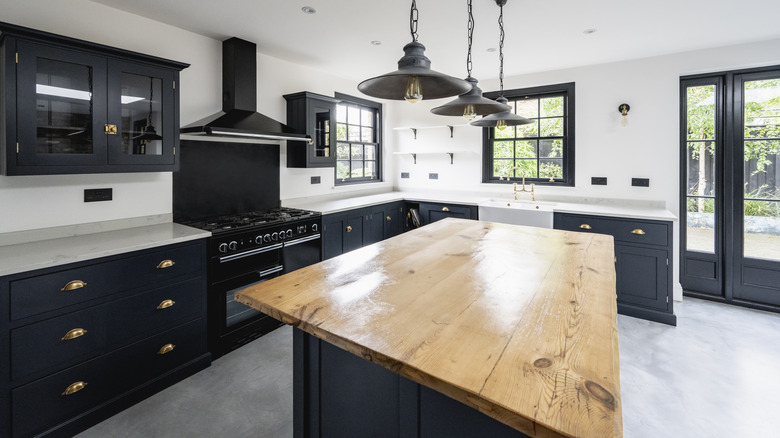 A kitchen with black cabinets, white perimeter countertops, and a wood-topped island