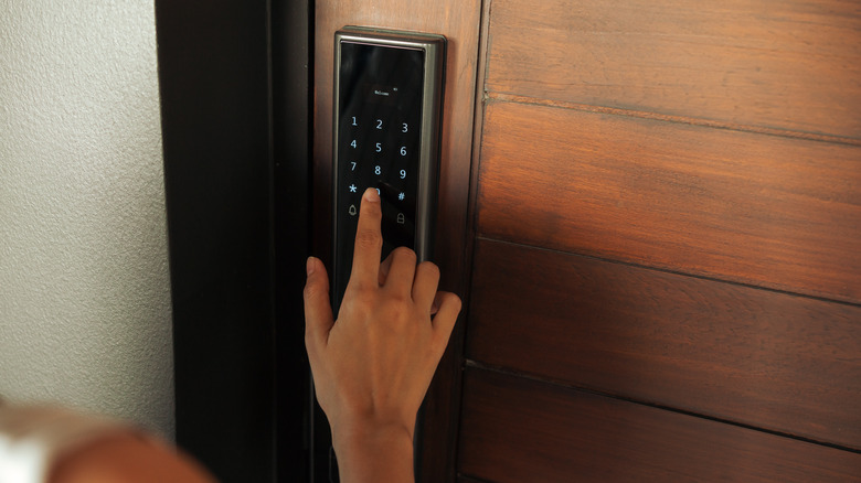 A hand pressing down the digital controls of a front door smart lock.