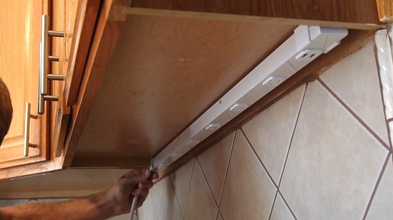 person installing under-cabinet outlet strip in kitchen