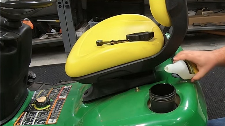 Person adding fuel stabilizer into a mower's fuel tank