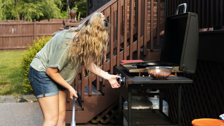 A person turning on the burner for a propane grill with tanks nearby