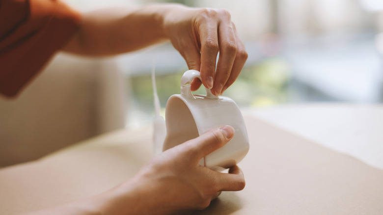 A person mending a broken cup with a blurred tube of super glue in the background