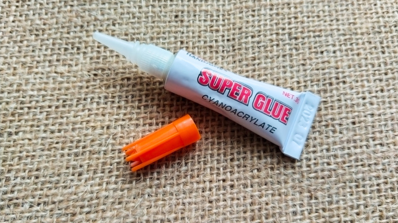 An opened tube of super glue laying on a hessian-covered table