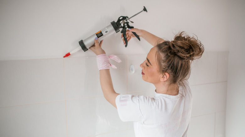 Woman using caulking gun on a white wall