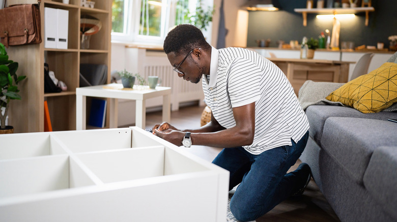 A young man assembling furniture in his apartment