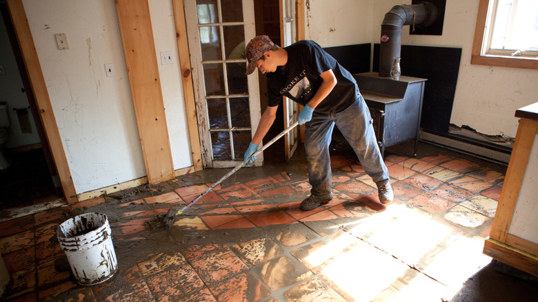 A man cleans mud off a tile floor after severe flooding in his home